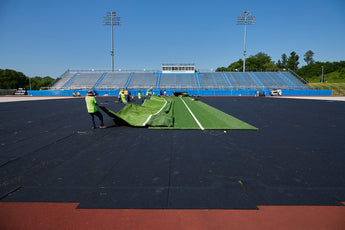 Synthetic turf being rolled out over black REGUPOL abzorb shock pad at a stadium installation