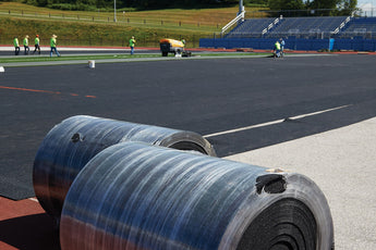 Rolls of REGUPOL abzorb shock pad with installed pad covering a stadium field